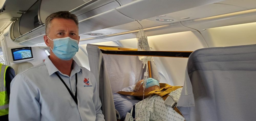 Medizinische. Mann steht neben Patienten im Bett im Flugzeug.